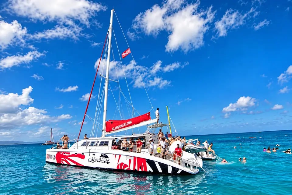Catamarã navegando em mar azul-turquesa com pessoas a bordo